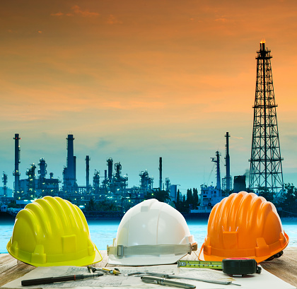 safety helmet on engineer working table against oil refinery plant background